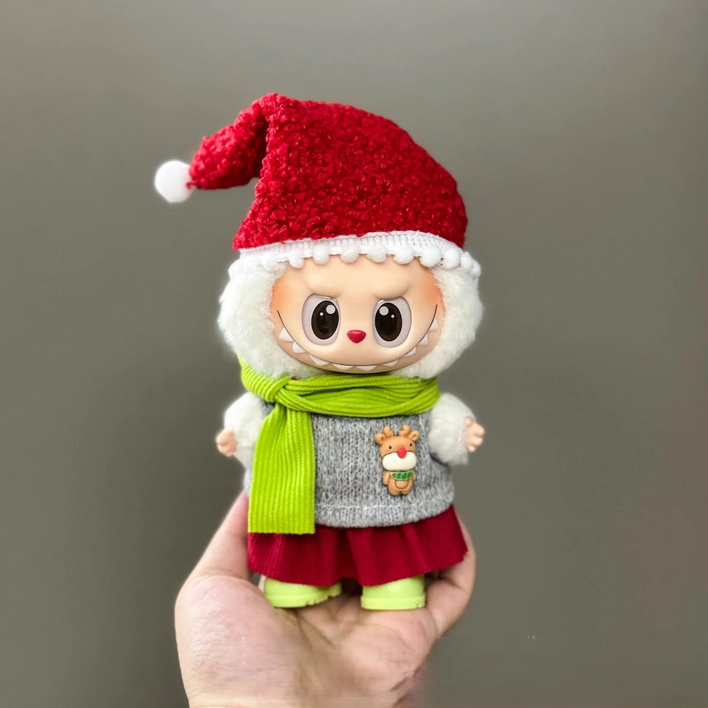 Small plush toy with a red Santa hat, green scarf, and gray sweater held in a hand against a plain background.