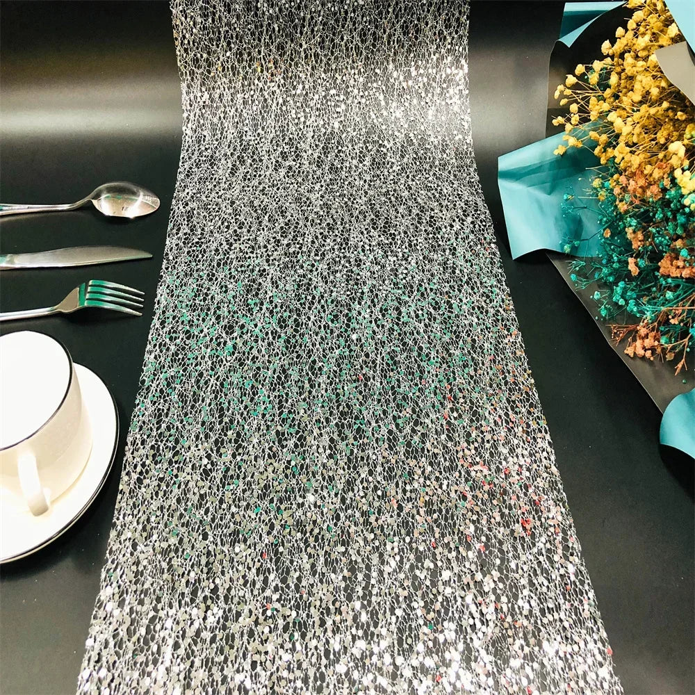 Silver sequin table runner on a black table with cutlery and flowers.