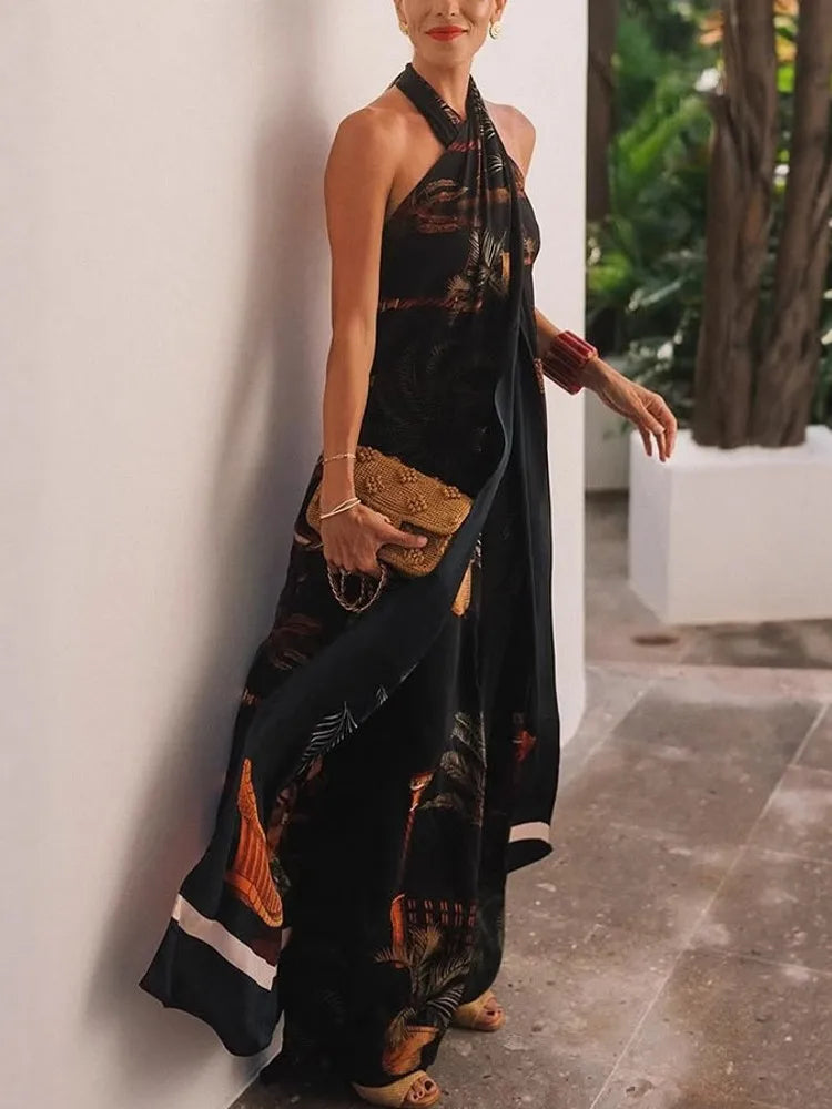 Woman in a black patterned dress holding a clutch against a white wall with greenery.