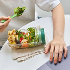 Person holding a jar of salad with a side of fried food on a white surface.