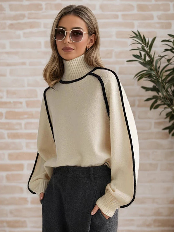 Woman wearing a cream sweater with black trim against a brick wall.