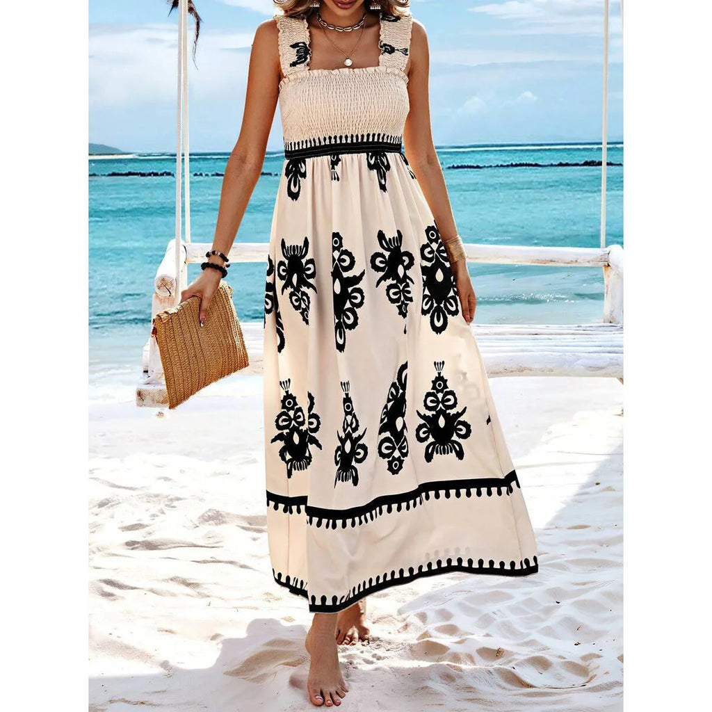 Woman in a long dress with black patterns standing on a beach.