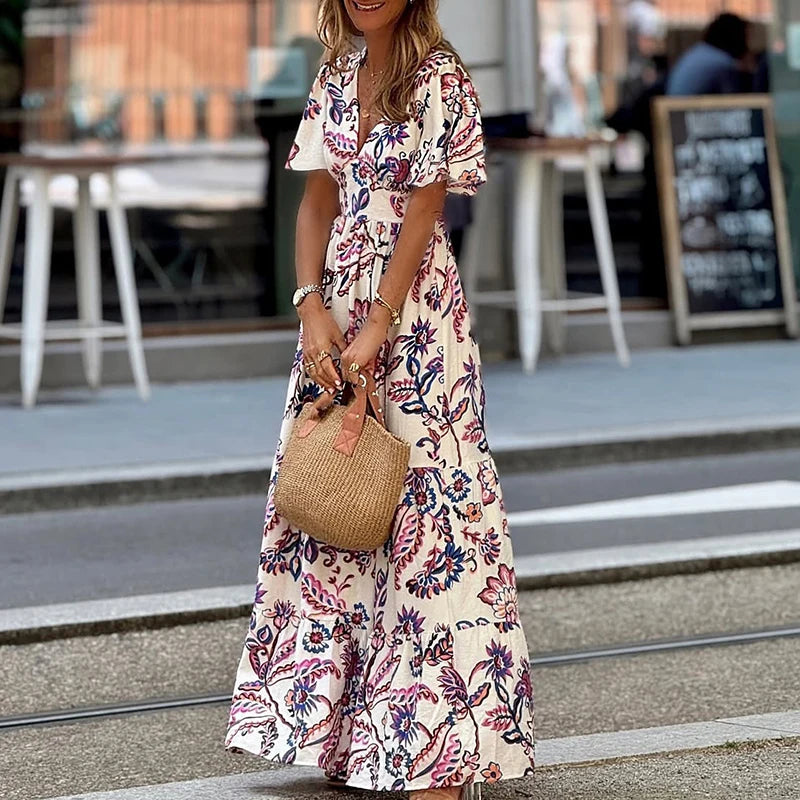 Woman in a floral dress holding a straw bag on a street.