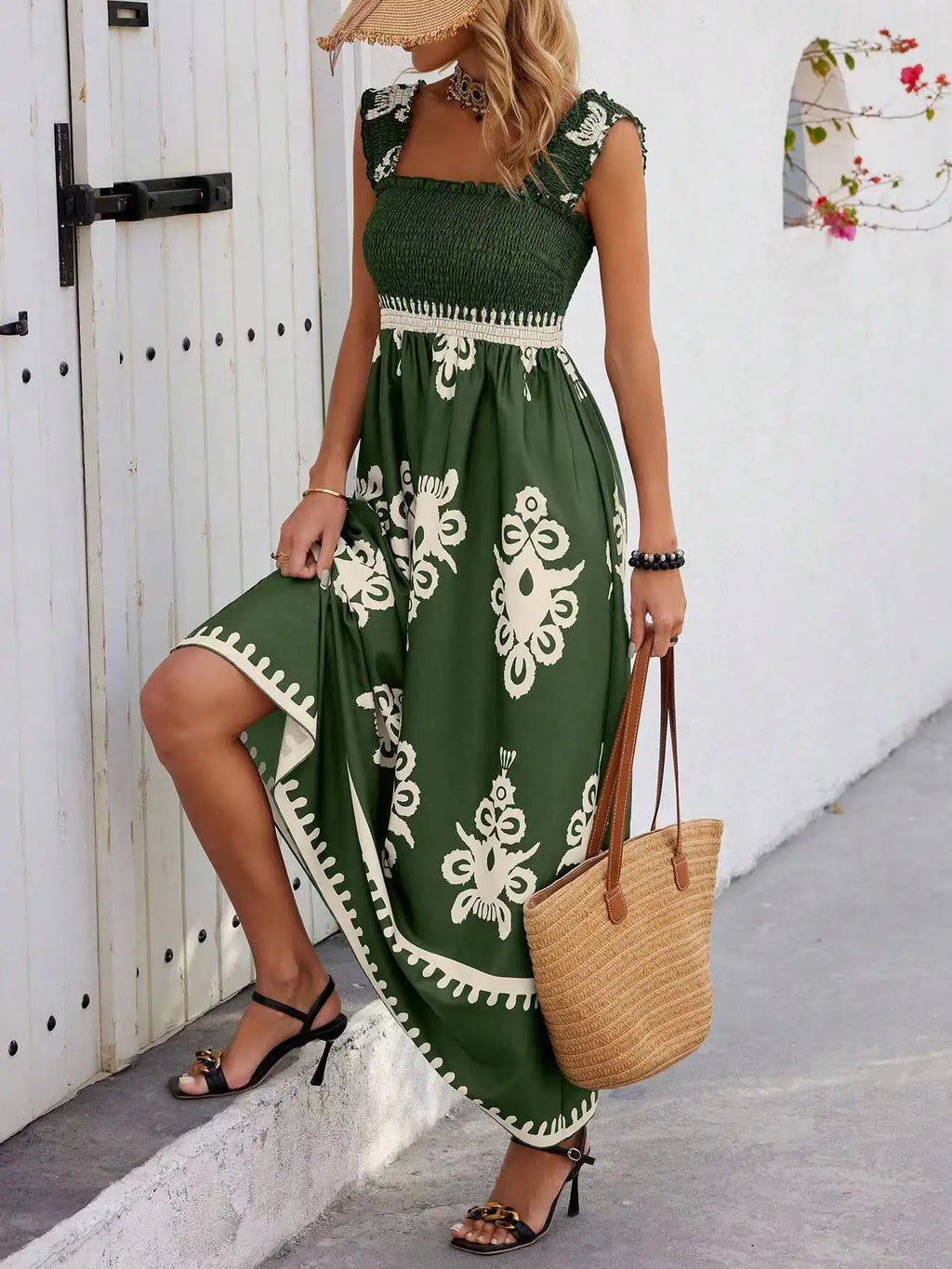 Woman wearing a green dress with white patterns, holding a straw bag, against a white wall.