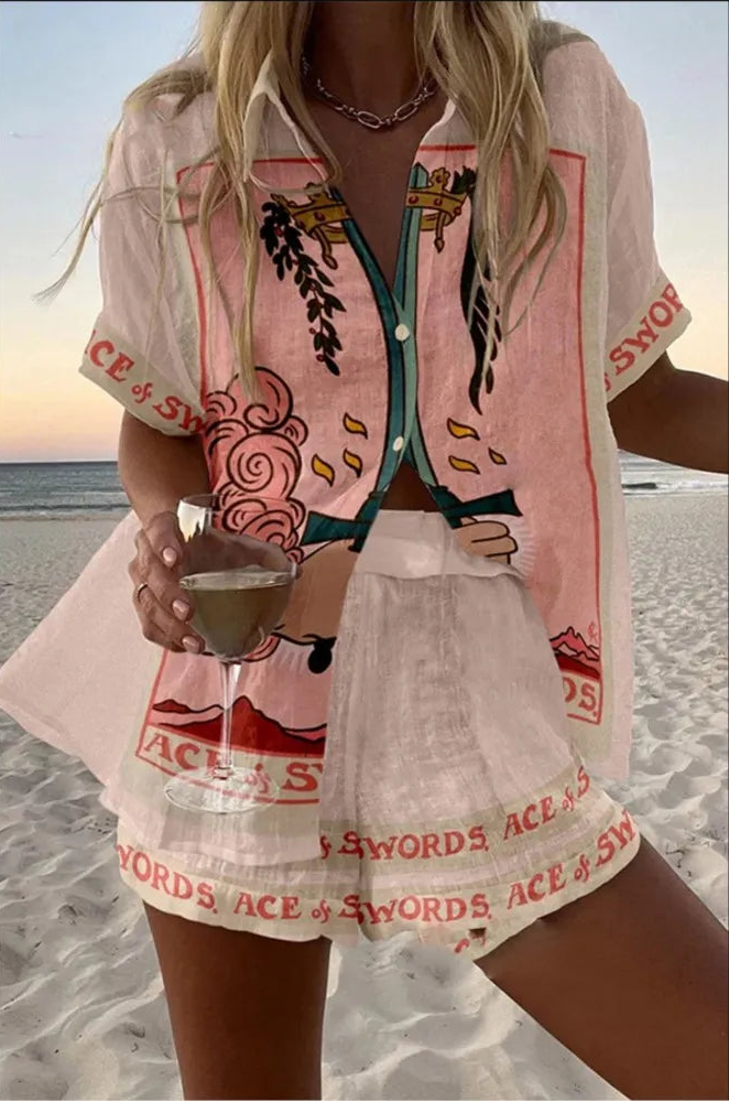Person wearing a colorful shirt and shorts with 'ACE of SWORDS' text on a beach.