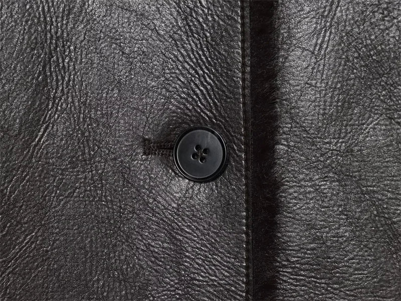 Close-up of a textured black leather coat with a button.