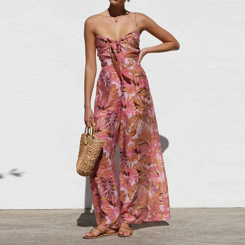 Woman wearing a pink floral jumpsuit holding a straw bag against a white background