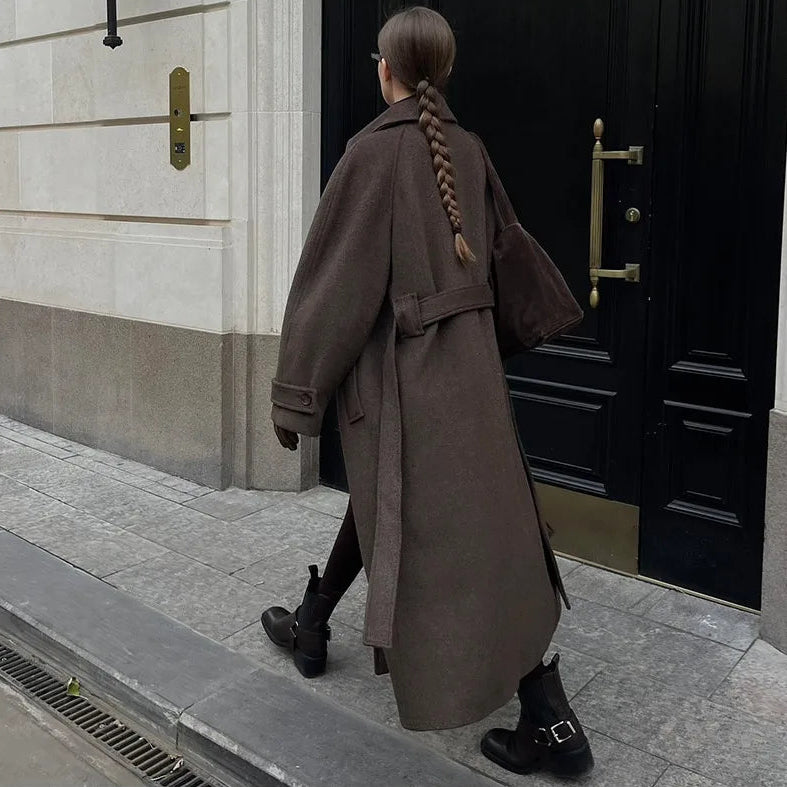 Person wearing a long brown coat walking towards a black door.