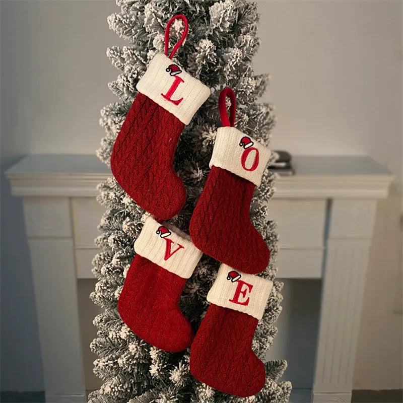 Red Christmas stockings with white letters hanging on a decorated tree.