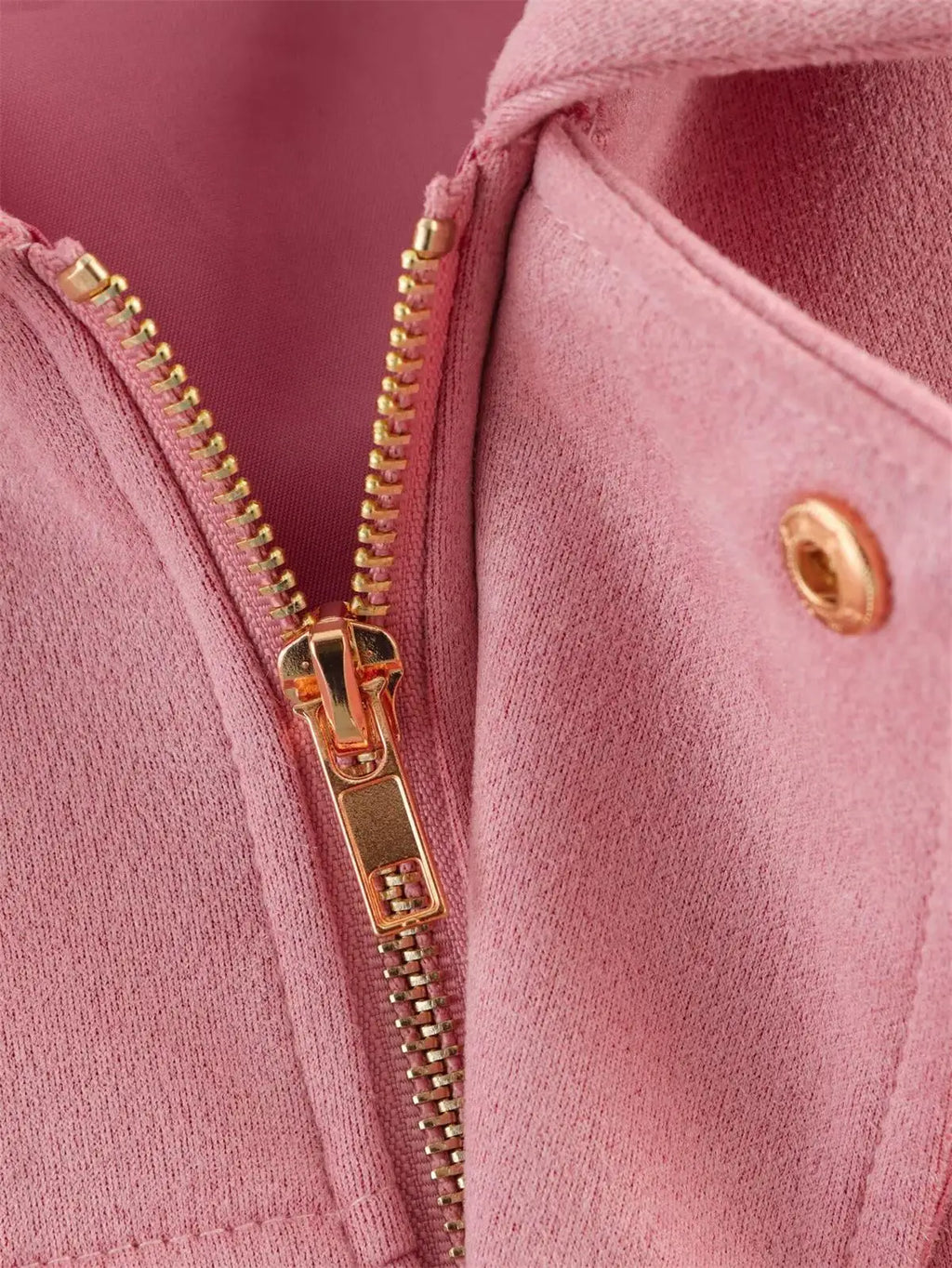 Close-up of a pink jacket with a gold zipper and button.