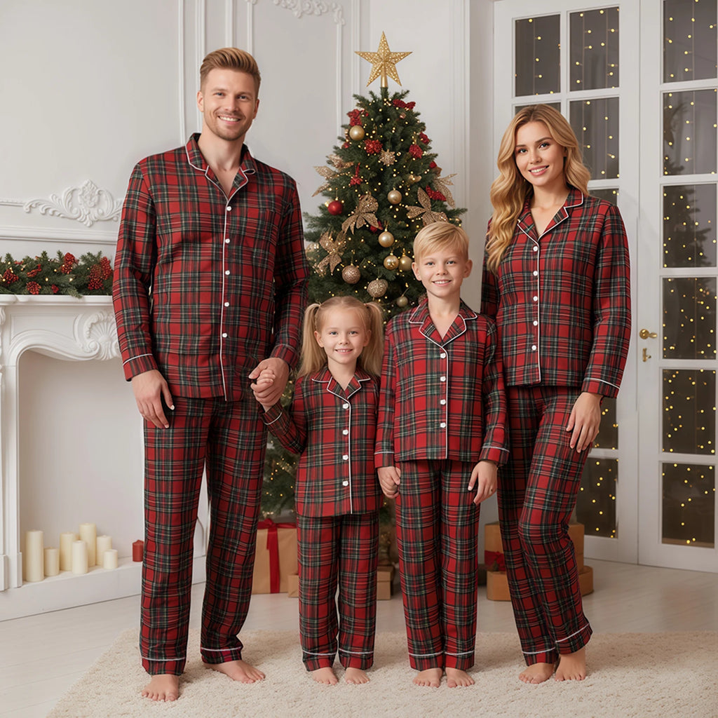 Family of four wearing matching red plaid pajamas in a festive room with a Christmas tree.