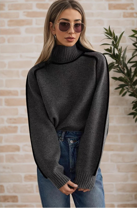 Woman wearing a dark gray turtleneck sweater and sunglasses against a brick wall.