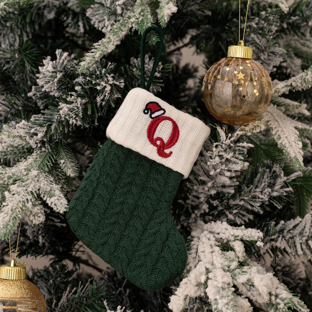 Green Christmas stocking with a red letter 'Q' and white cuff hanging on a decorated tree.