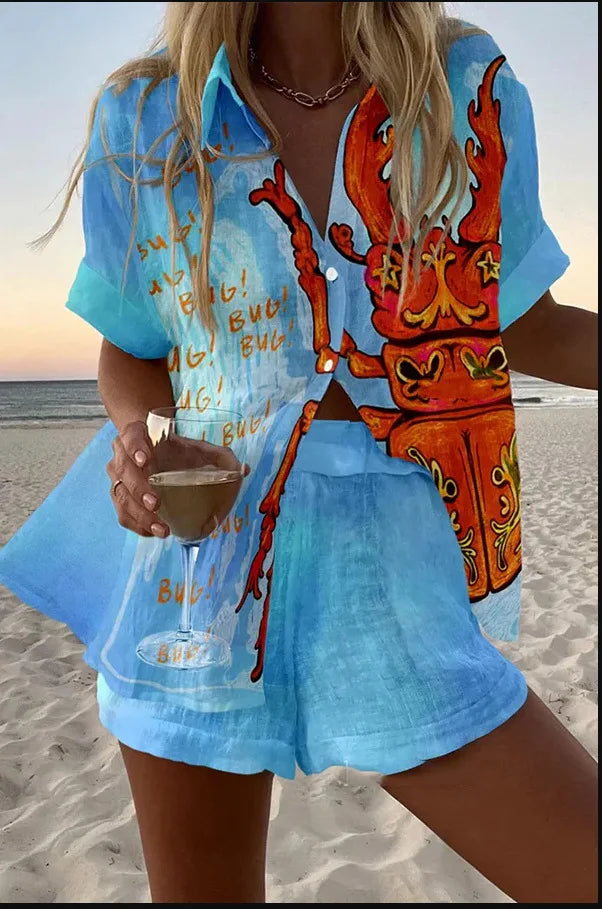 Person wearing a blue shirt with a colorful design and shorts, holding a drink on a beach.