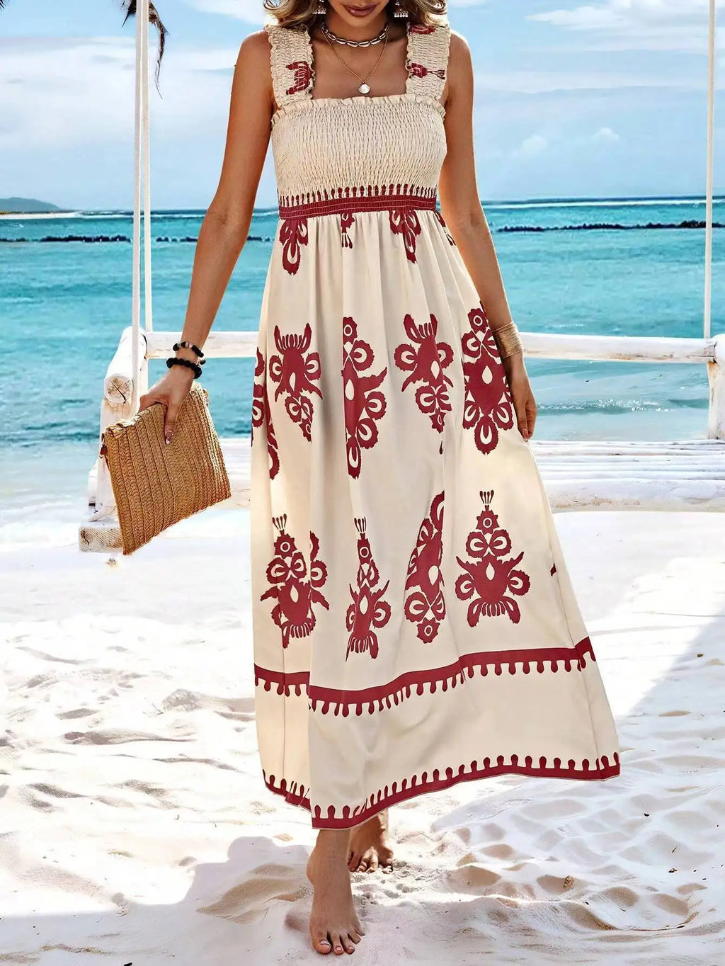 Woman in a long, patterned dress standing on a beach with ocean view