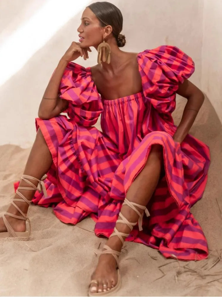 Woman wearing a vibrant pink and purple dress with puffed sleeves, sitting on a neutral background.
