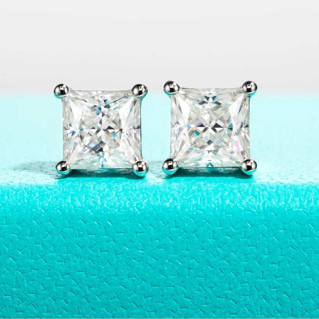 Square-cut stud earrings on a turquoise surface with 'Anu Jewel' branding.