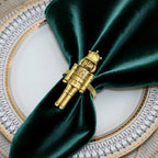 Gold nutcracker napkin ring on a green napkin with a decorative plate in the background