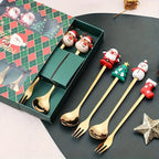Set of gold Christmas-themed spoons and forks with decorative handles on a dark surface.