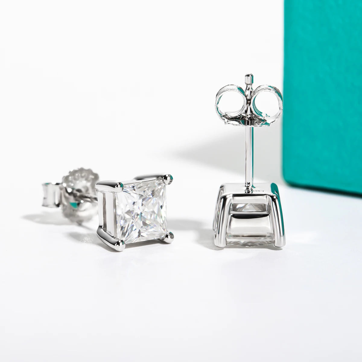 Pair of diamond stud earrings on a white background with a teal box.