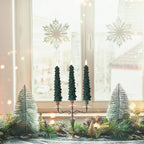 Decorative Christmas setup with trees and a candelabra in front of a window with snowflake decorations.