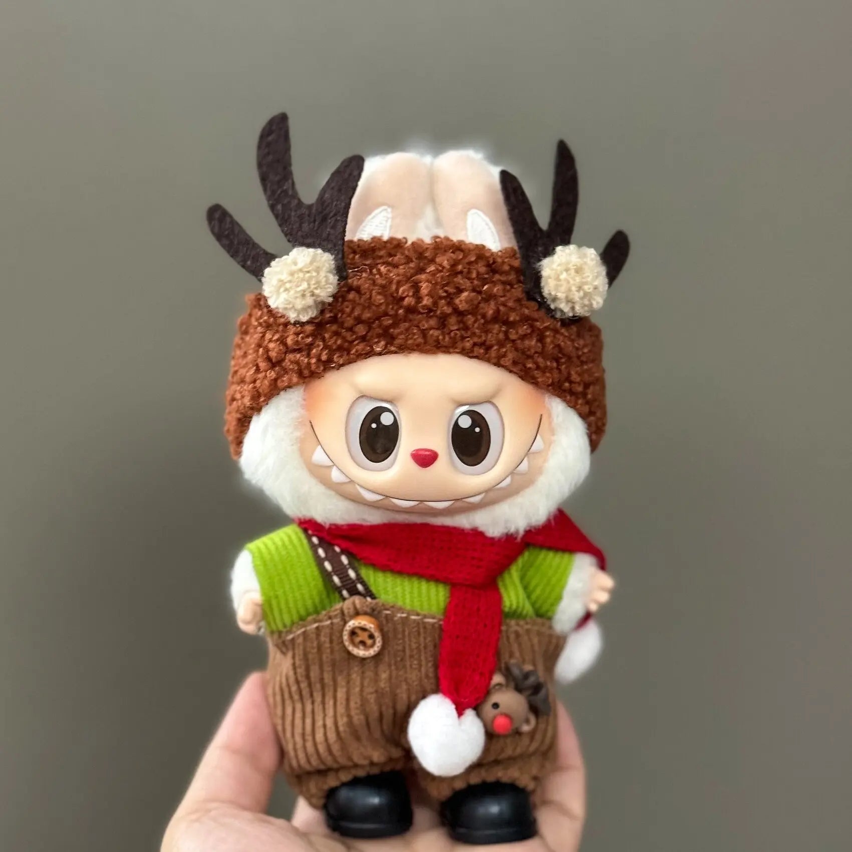 Toy figure of a reindeer with a brown hat, green sweater, and red scarf on a gray background