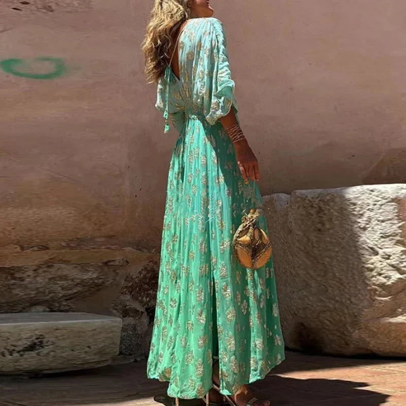 Woman in a green floral dress standing against a textured wall.