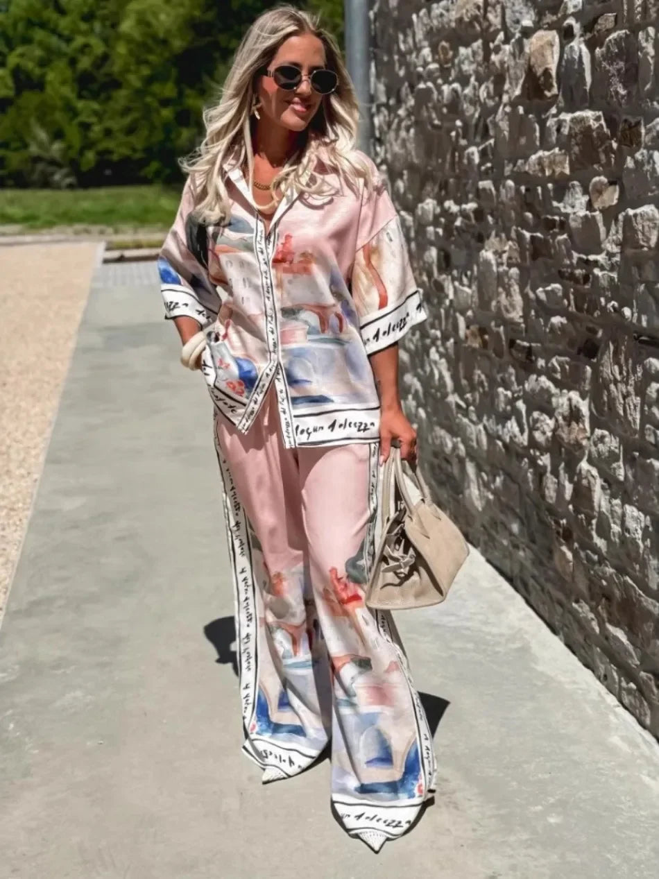 Woman wearing a colorful outfit with a patterned shirt and pants, standing against a stone wall.