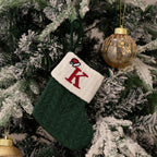 Green knitted Christmas stocking with red letter 'K' ornament on a decorated tree.