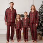 Family of four wearing red plaid pajamas standing in a room with a Christmas tree.