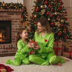 Woman and child in matching green pajamas exchanging gifts in front of a decorated Christmas tree.