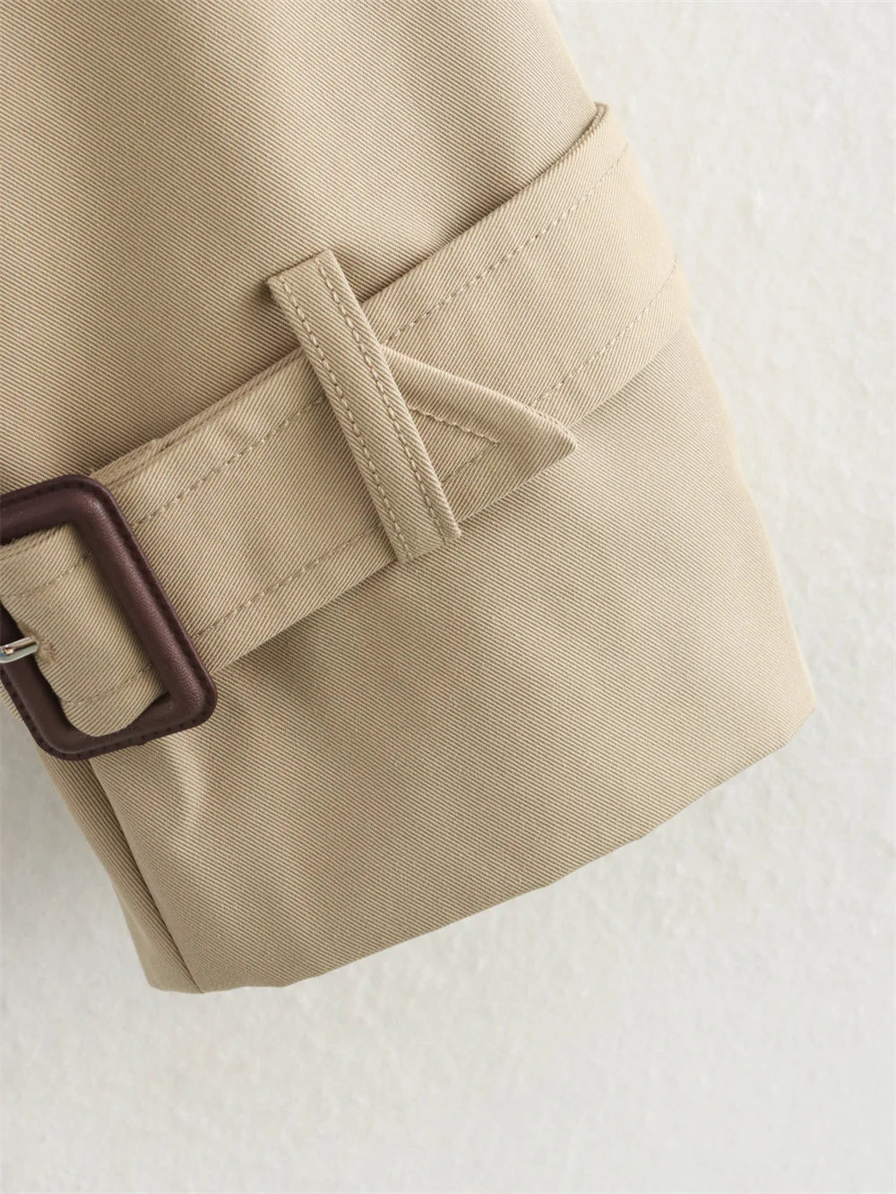 Close-up of a beige trench coat with a brown buckle on a light background