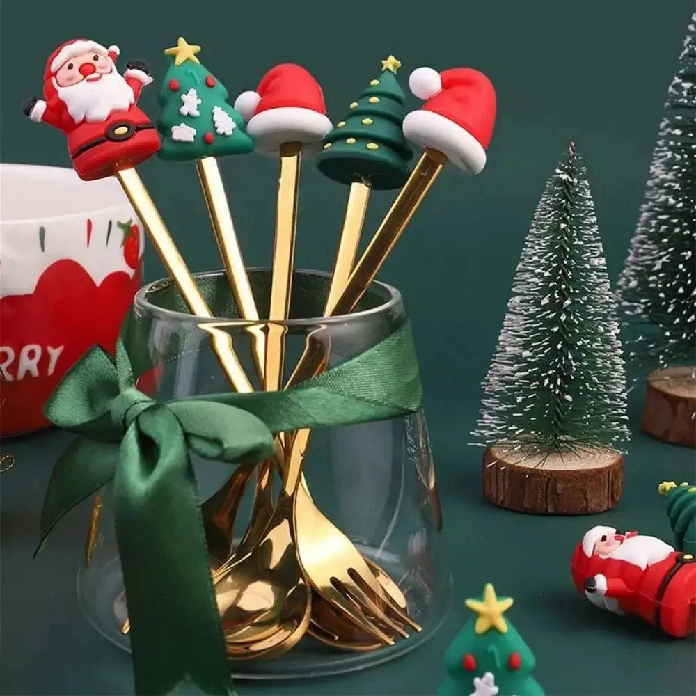 Set of gold Christmas-themed spoons in a glass jar with decorative items on a green background