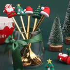 Set of gold Christmas-themed spoons in a glass jar with decorative items on a green background