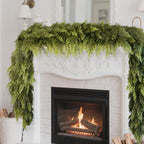 Artificial Norfolk cedar garland hanging over a white fireplace with a burning fire.