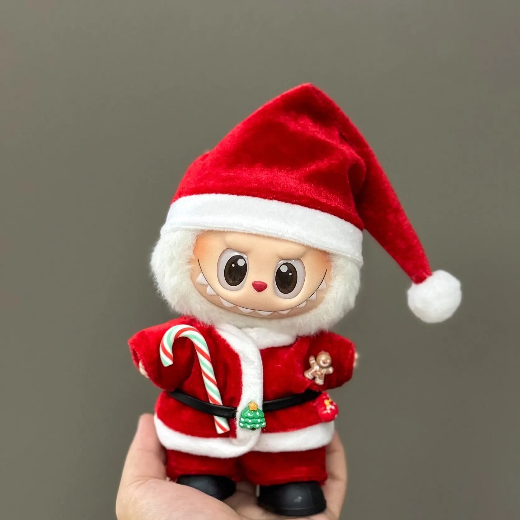 Small plush toy dressed as Santa Claus holding a candy cane against a plain background