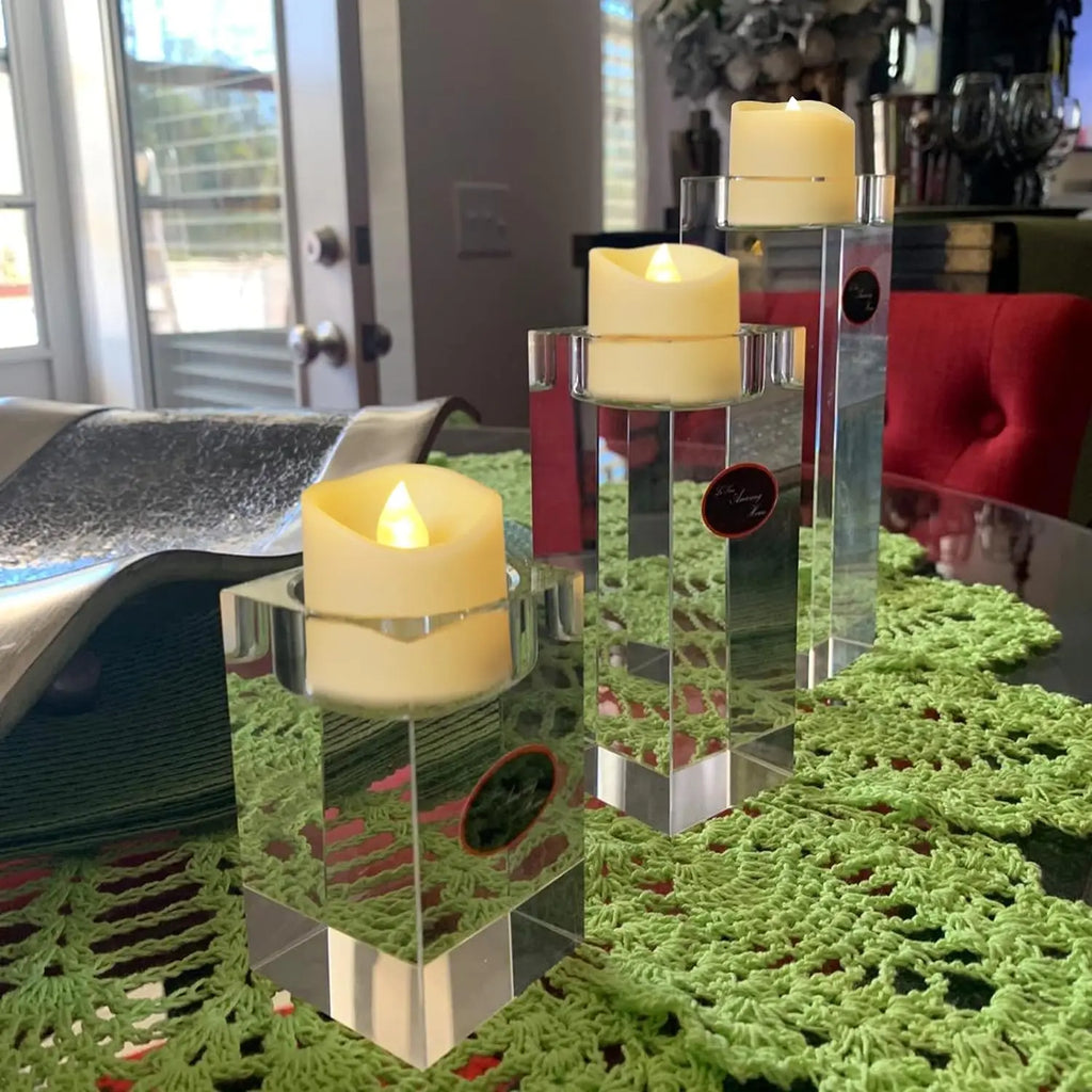 Decorative candles in clear glass holders on a green textured surface with a blurred indoor background.