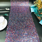 Colorful sequin table runner on a black table with silverware and a cup.