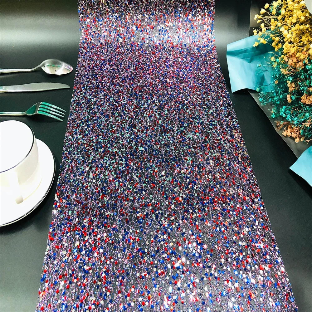 Colorful sequin table runner on a black table with silverware and a cup.