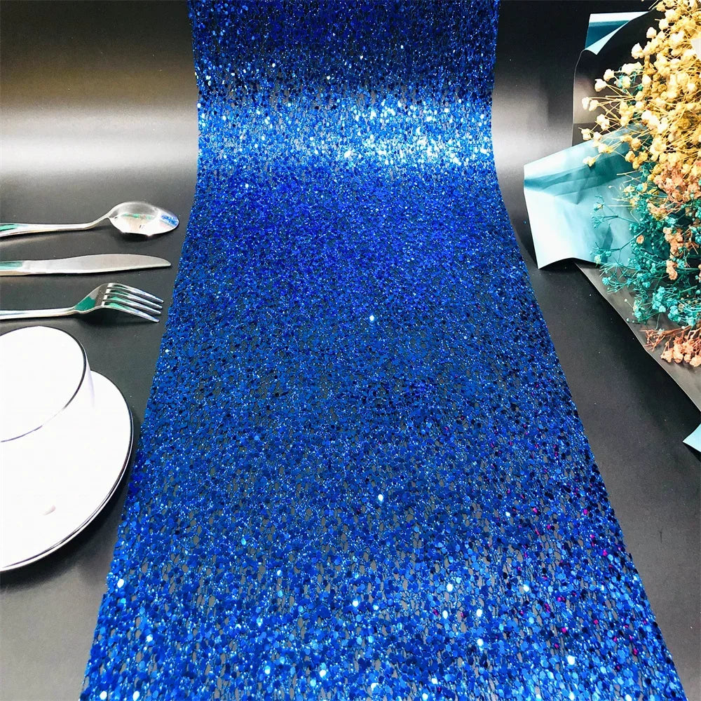 Blue glittery table runner on a black surface with silverware and plates.