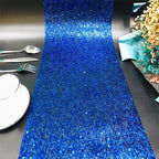 Blue glittery table runner on a black surface with silverware and plates.