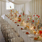 Elegant wedding reception setup with long table, chairs, floral arrangements, and candles.
