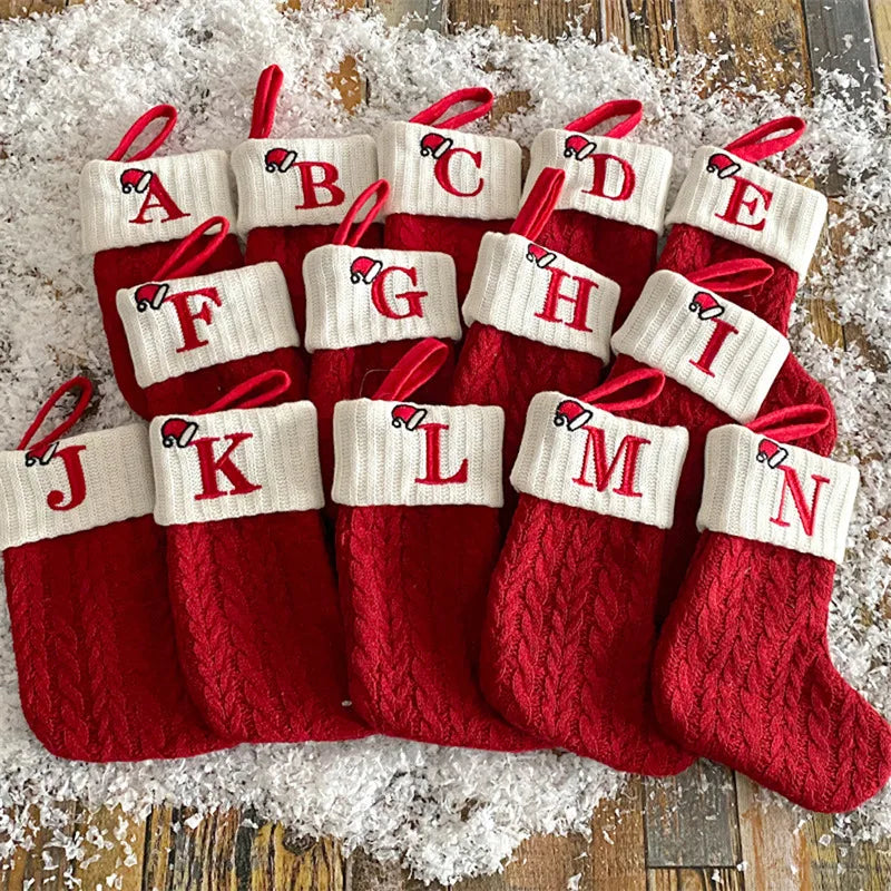 Set of red Christmas stockings with white letter tags on a wooden surface.