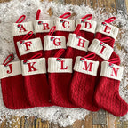 Set of red Christmas stockings with white letter tags on a wooden surface.