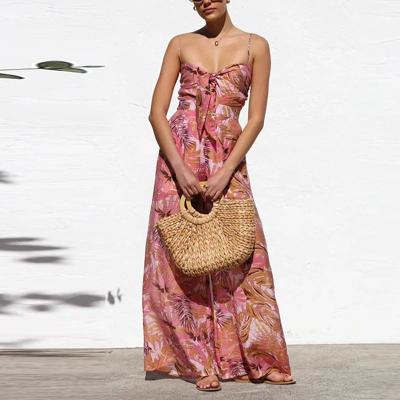 Woman in a pink floral dress holding a woven bag against a white wall.