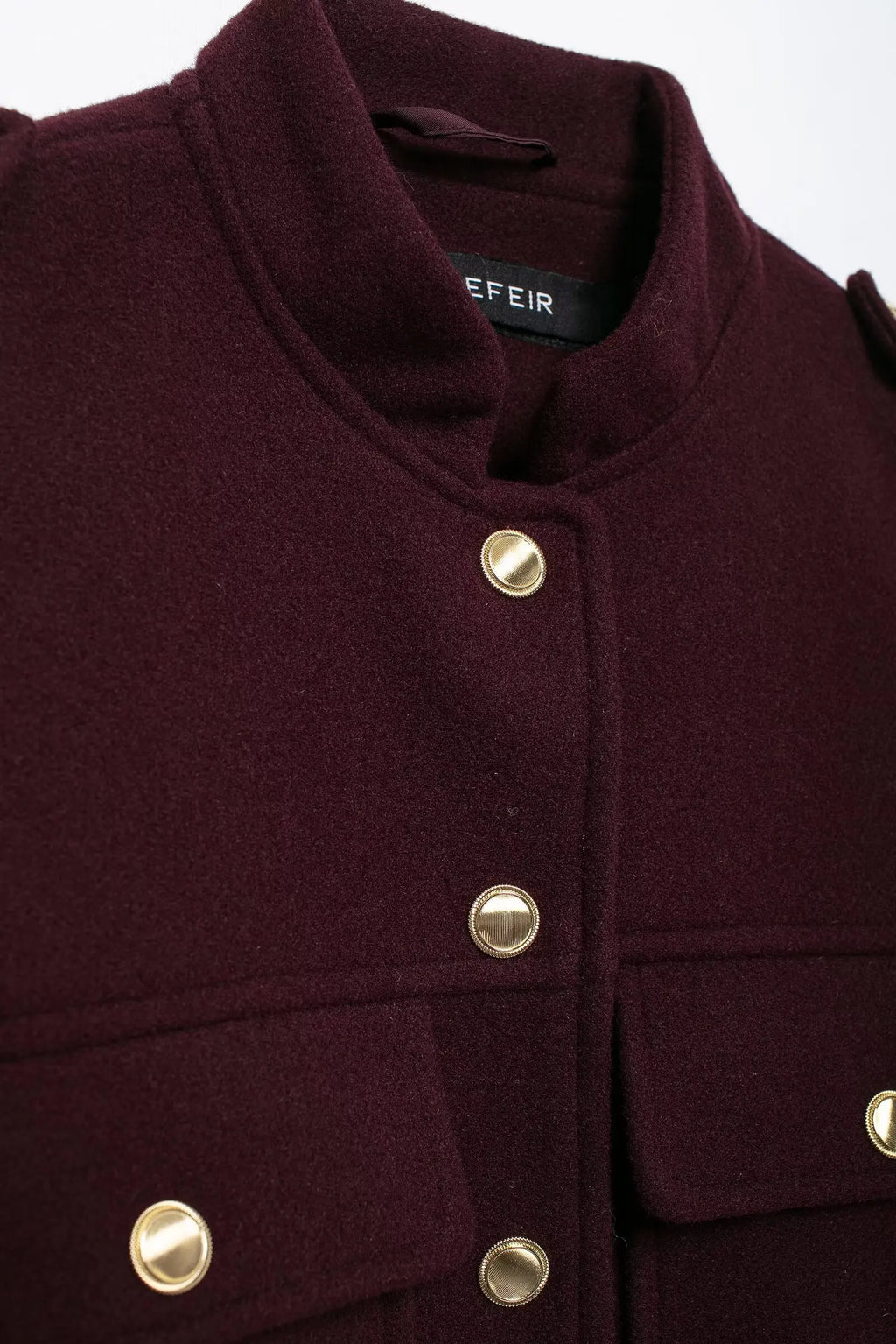 Close-up of a dark purple coat with gold buttons on a white background