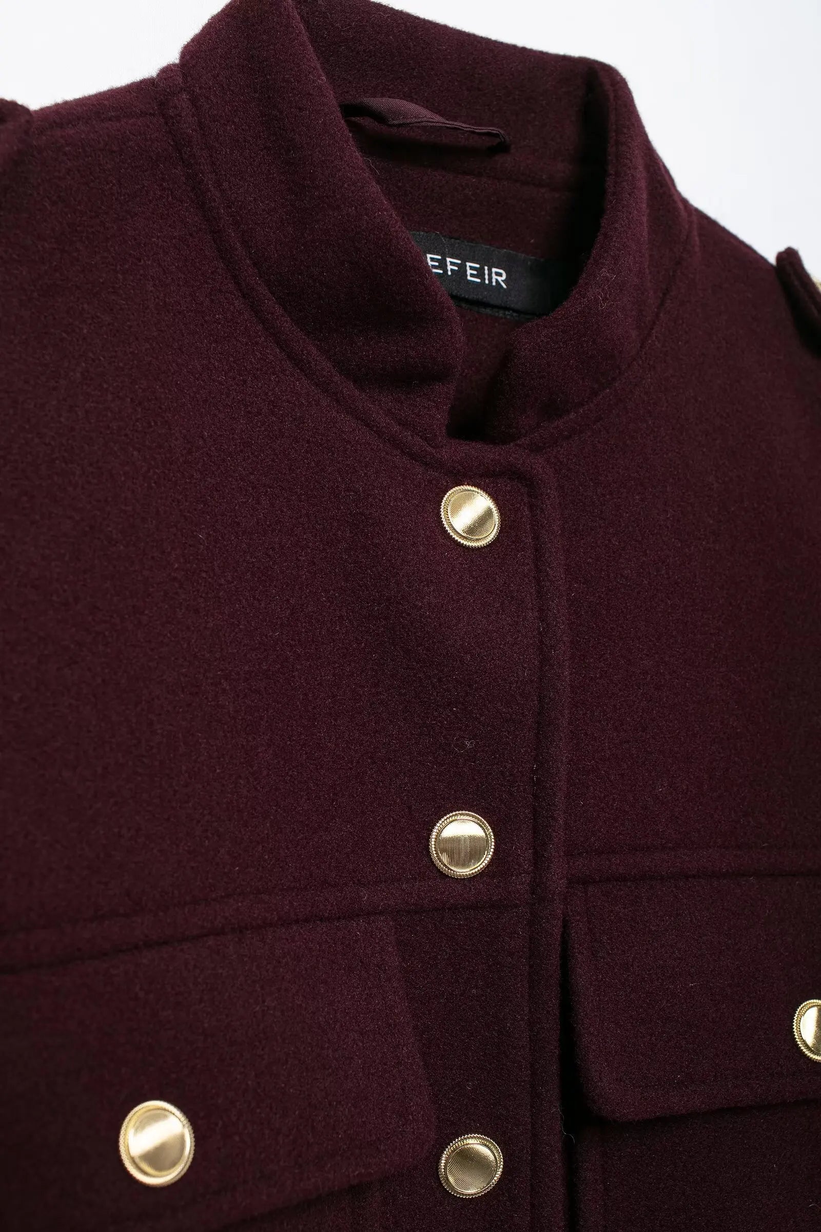 Close-up of a dark purple coat with gold buttons on a white background