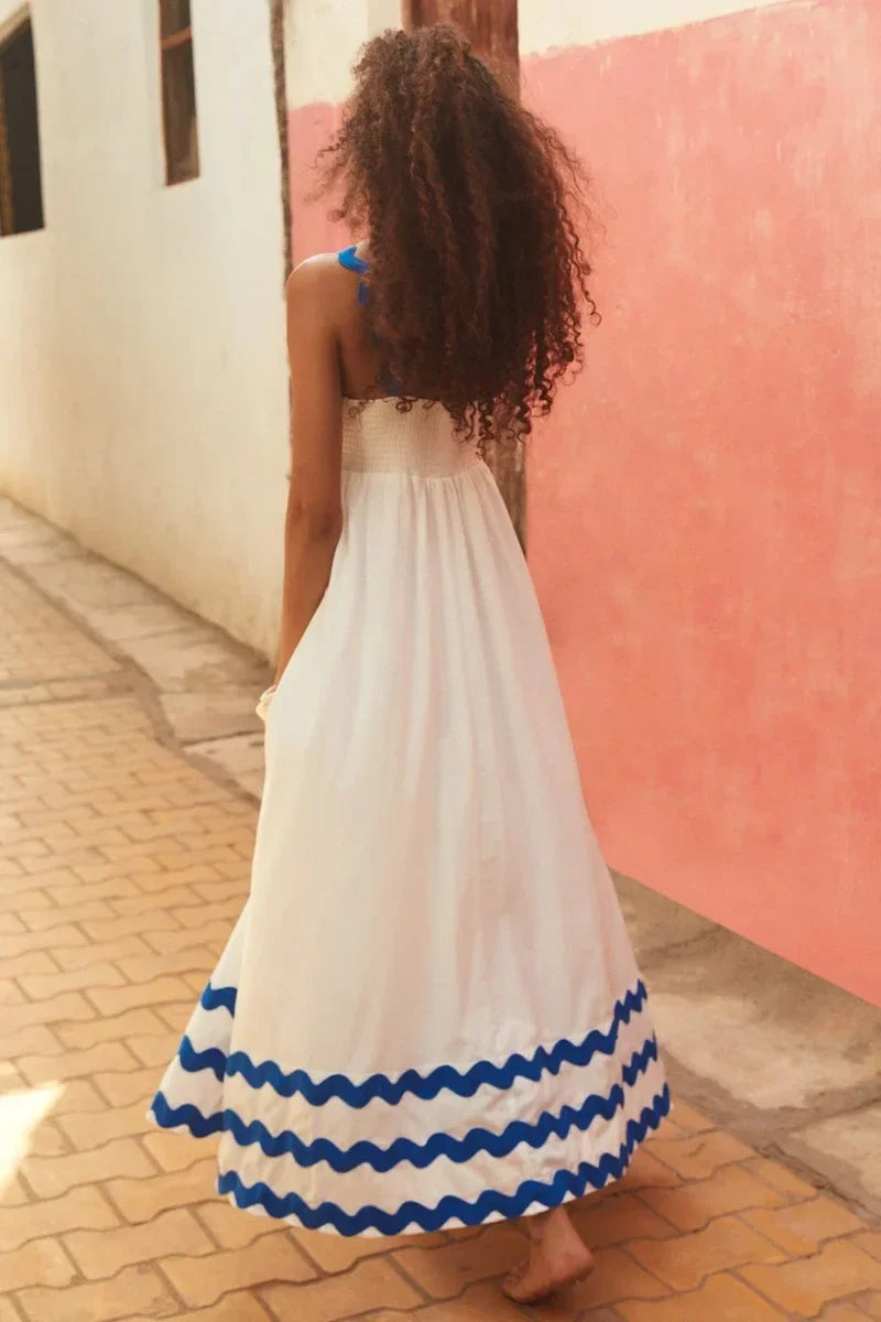 Woman in a white dress with blue trim walking along a street.