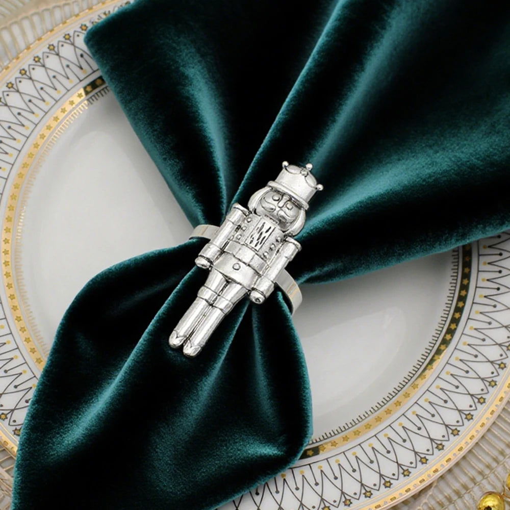 Silver nutcracker napkin ring on a green napkin with a decorative plate in the background
