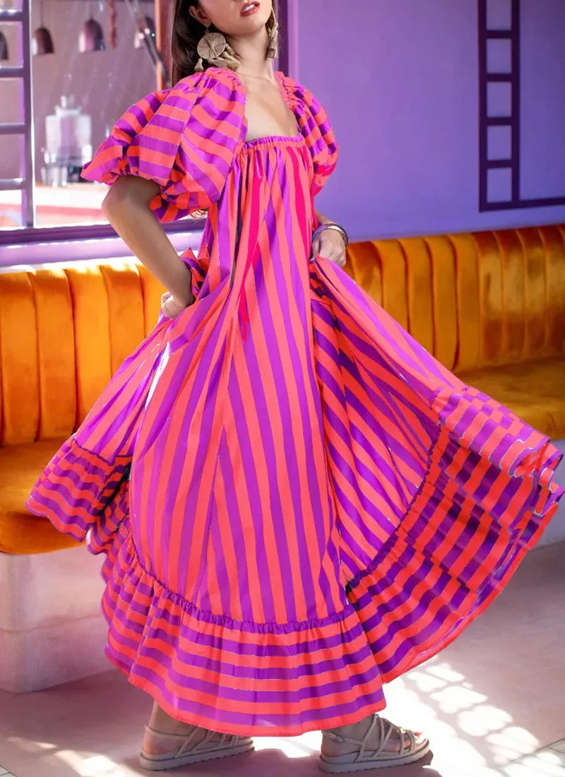 Woman wearing a vibrant pink and purple striped dress in a room with orange couch and white walls.